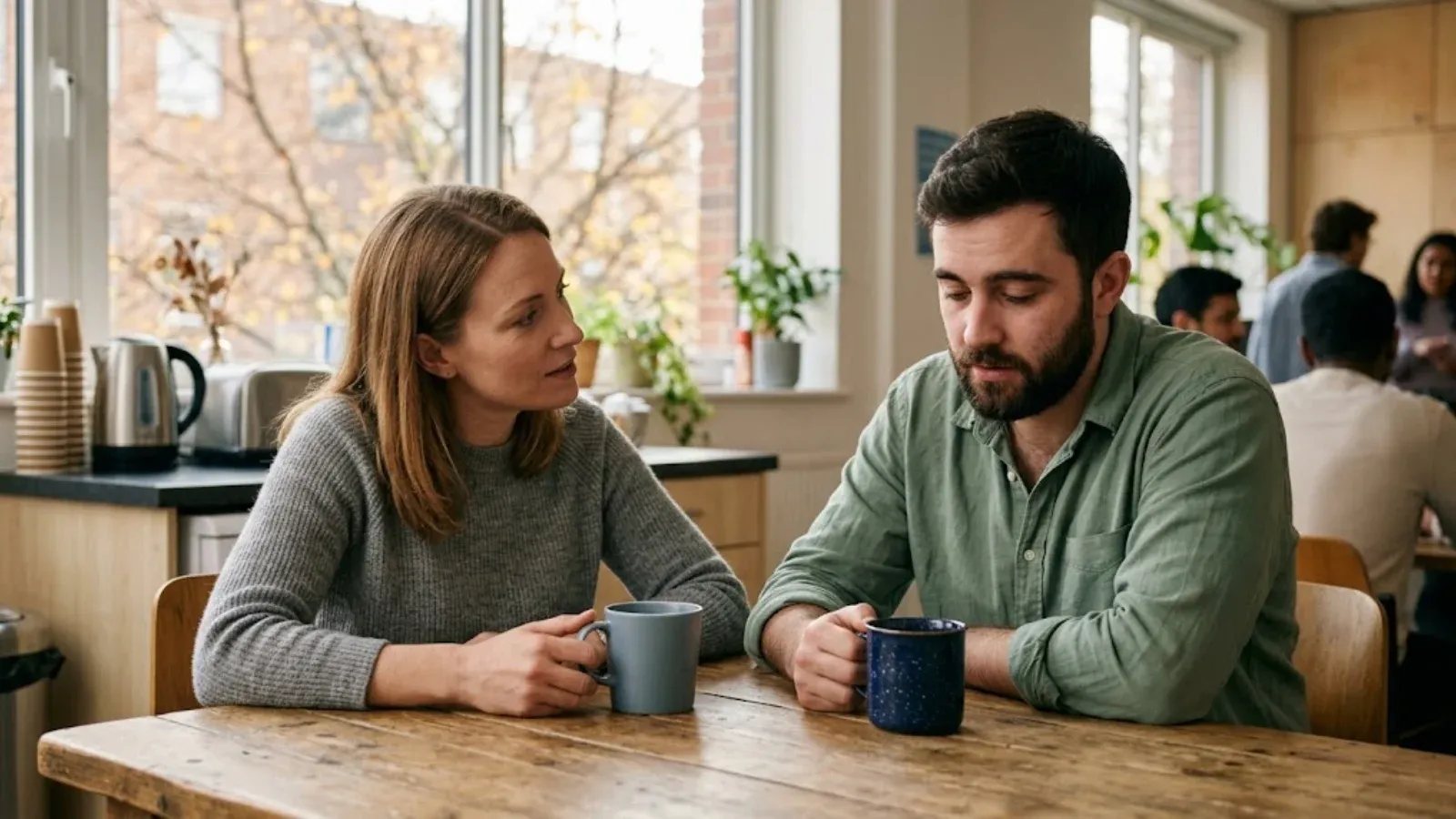 Two coworkers talking quietly over coffee at a break room table
