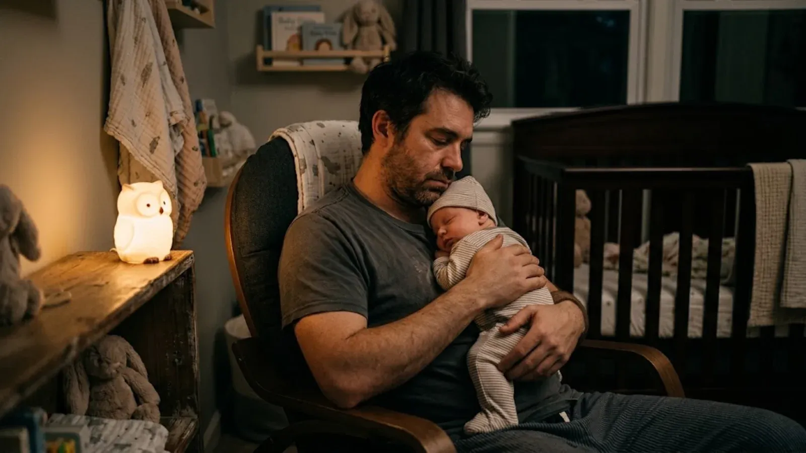 A tired new father holding his sleeping newborn in a dim nursery at night