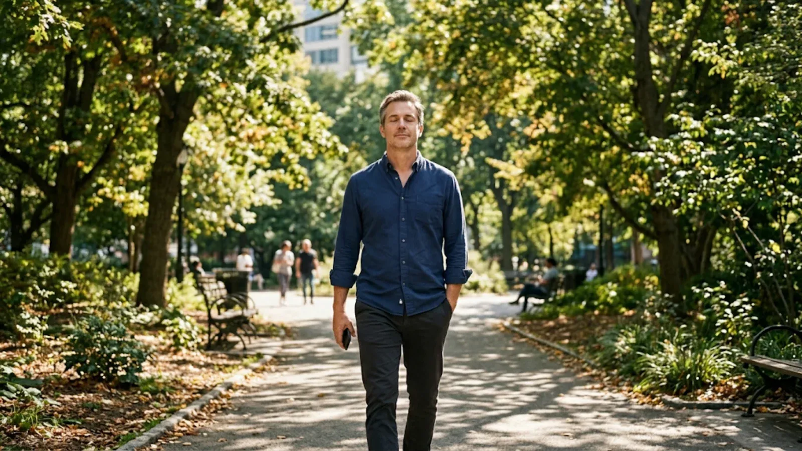 Man in business-casual clothes taking a calm midday walk on a sunlit park path, breathing deeply