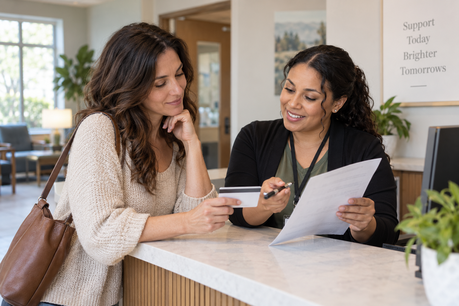 Patient and clinic coordinator review an insurance card and benefits paperwork at a reception desk.
